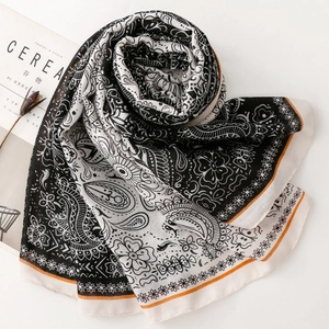 Flat lay of black and white Paisley scarf with orange trim and lifestyle props