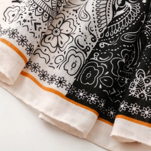 Close-up of paisley pattern on cotton scarf with black and white motifs and orange border