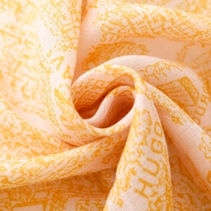 Macro view of warm orange scarf fabric showing retro map print and breathable texture