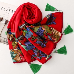Red ethnic floral shawl with exquisite embroidery and green metal cap tassels on white desk