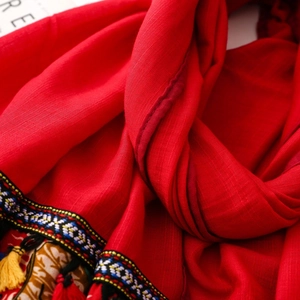 Macro detail of red ethnic scarf showing intricate embroidery and colorful tassel fringe