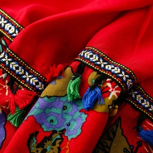 Detail of red ethnic shawl featuring rainbow geometric embroidery and colorful tassels