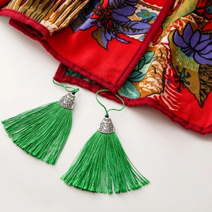 Close-up of red ethnic shawl featuring green tassels and engraved silver metal caps