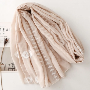 Detail shot of delicate white floral embroidery on beige ethnic style scarf fabric