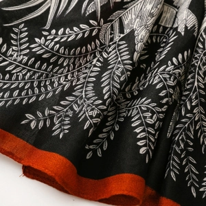 Detailed macro view of tropical leaf print on black cotton scarf with red stitched edges