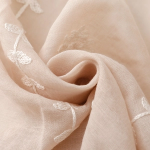 Macro detail of intricate white floral embroidery on premium beige silk gauze fabric