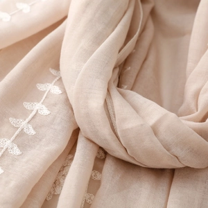 Close-up of beige linen scarf featuring white leaf embroidery and soft woven texture