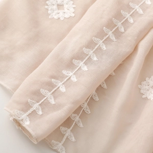 Detailed close-up of white floral embroidery on beige lightweight textile scarf