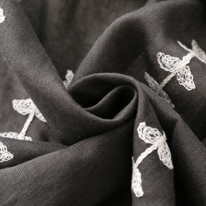 Detailed close-up of ethnic floral embroidery on dark grey linen textured fabric scarf