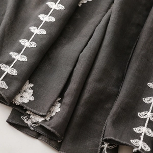 Detail of dark gray scarf featuring intricate white leaf embroidery and premium rolled edges