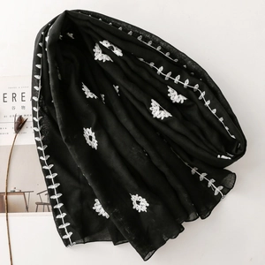 Close-up of intricate white floral embroidery on premium black shawl fabric texture