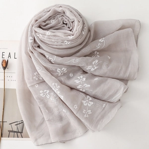 Detail of light gray cotton linen scarf with white daisy floral embroidery and soft texture