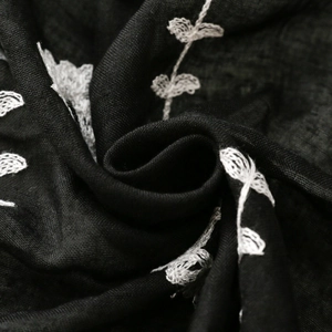 Detailed macro view of white plant leaf embroidery on soft black linen texture fabric