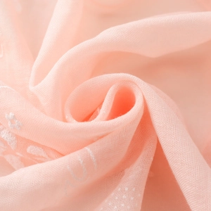 Macro shot of peach pink cotton linen scarf with elegant floral embroidery and texture