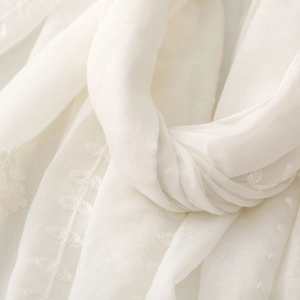 Detailed macro view of cream-white ethnic embroidery on lightweight textured scarf fabric