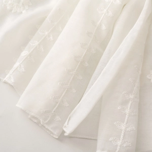Detailed close-up of white ethnic embroidery with leaf patterns on cotton-linen fabric