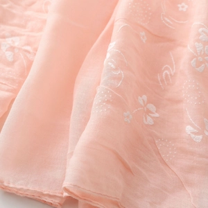 Macro detail of soft pink linen scarf showing delicate white floral embroidery and texture