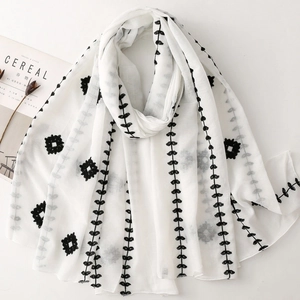 Detail of minimalist cream scarf with black ethnic leaf embroidery and tassel edges
