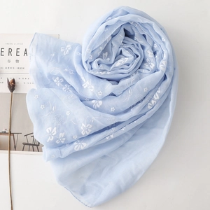 Detailed embroidery on light blue linen scarf with white floral patterns on white surface