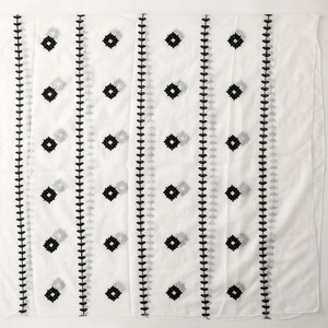 Detail of white embroidery scarf featuring black leaf patterns and geometric diamonds