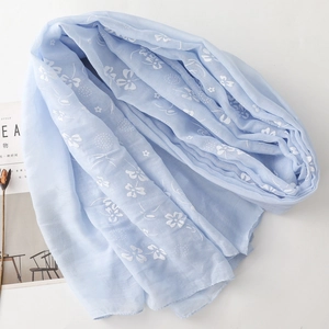 Detail of light blue linen scarf featuring delicate white floral embroidery and airy texture