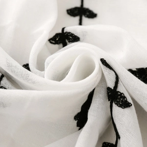 Detailed macro view of white scarf fabric with black floral embroidery and soft texture