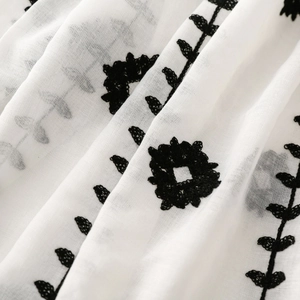 Detailed macro view of black floral embroidery on a white woven linen fabric scarf
