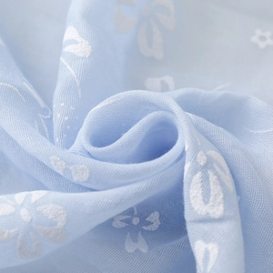 Detail view of light blue embroidery fabric with white floral patterns and soft texture