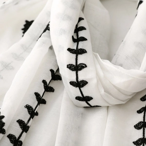 Close-up detail of white cotton linen scarf with black floral vine embroidery