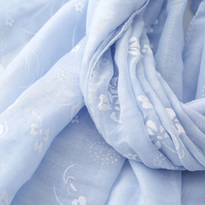 Detailed macro view of light blue cotton linen scarf with delicate white floral patterns