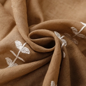 Detailed close-up of ethnic floral embroidery on soft caramel brown scarf fabric