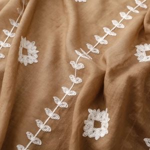 Detail of light brown scarf with intricate white floral embroidery and cotton texture