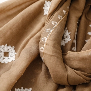 Close-up of ethnic white embroidery patterns on textured brown cotton linen scarf