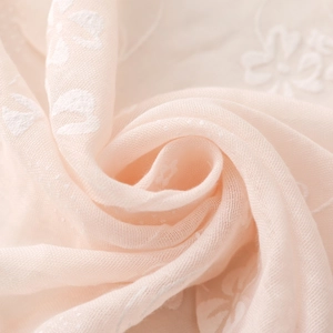 Macro shot of light pink scarf fabric with delicate white floral embroidery and dot texture