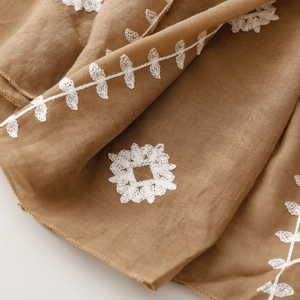 Detailed macro view of white floral embroidery on a brown linen fabric shawl