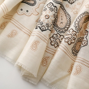 Dettaglio del motivo paisley vintage su sciarpa in cotone crema con bordi sfrangiati