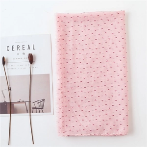 Écharpe rose en coton et lin avec motifs floraux rouges et bordures à franges sur un magazine