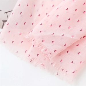 Détail d'une écharpe en coton et lin rose avec motifs de cœurs rouges et franges