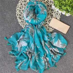 Detail of tropical palm leaf print on light blue linen scarf with decorative tassels