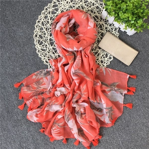 Detailed view of coral orange scarf featuring palm leaf prints and fine tassel fringes