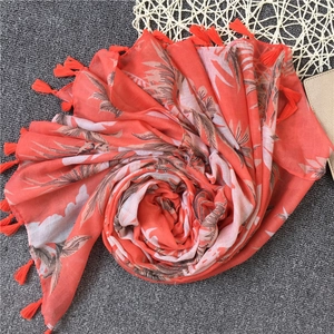 Close-up of tropical palm leaf print on orange linen scarf with tassel trim detail