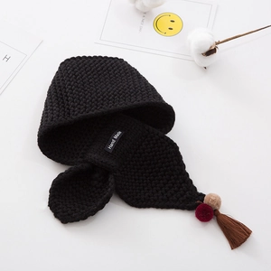 Detail of black knit scarf with handmade label and pompom fringe accents