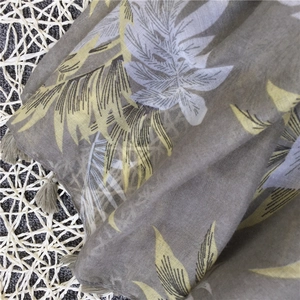Detail of yellow banana leaf print scarf with fringe tassels on woven mat background