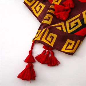 Close-up of red scarf featuring yellow Greek key patterns and multi-layered tassels