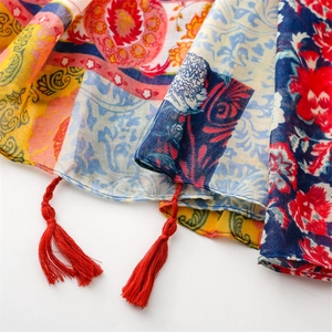Detail of ethnic paisley floral scarf featuring vibrant colors and red braided tassels