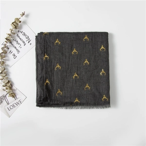 Detailed view of dark grey cotton scarf with golden reindeer print and tassel edges