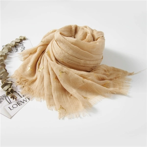 Detail of light brown linen scarf featuring gold reindeer prints and frayed fringe edges