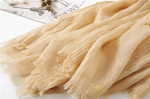 Detail of beige scarf with gold foil reindeer pattern and fringe edges in a cozy setup