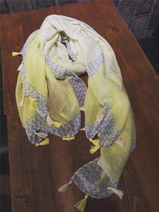 Detail view of yellow geometric pattern scarf with soft tassels on dark wood background
