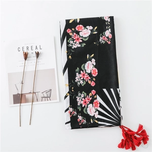 Détail d'une écharpe en lin imprimé floral avec un pompon rouge au coin